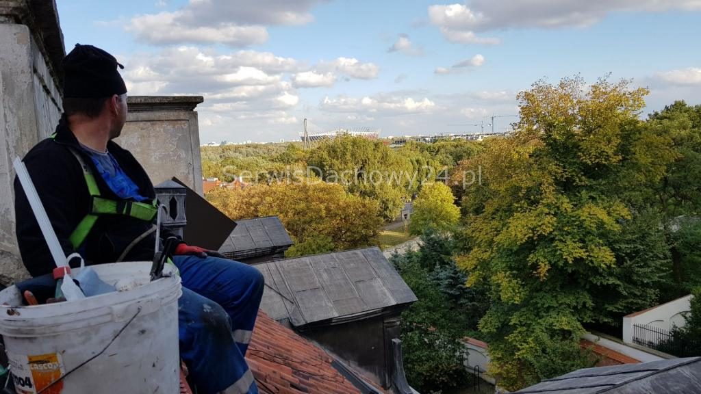 Dekarz na dachu nad zielenią Warszawy