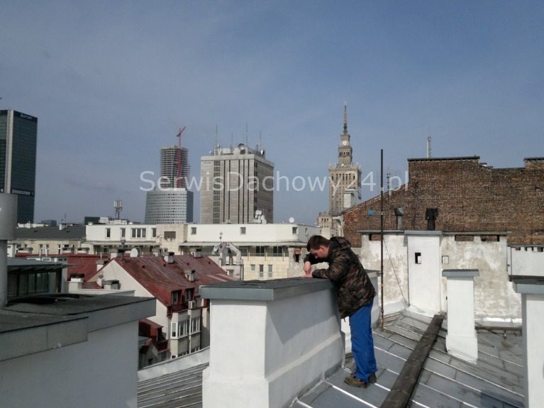 Dekarz na dachu kamienicy w centrum Warszawy, w tle Pałac Kultury i Nauki